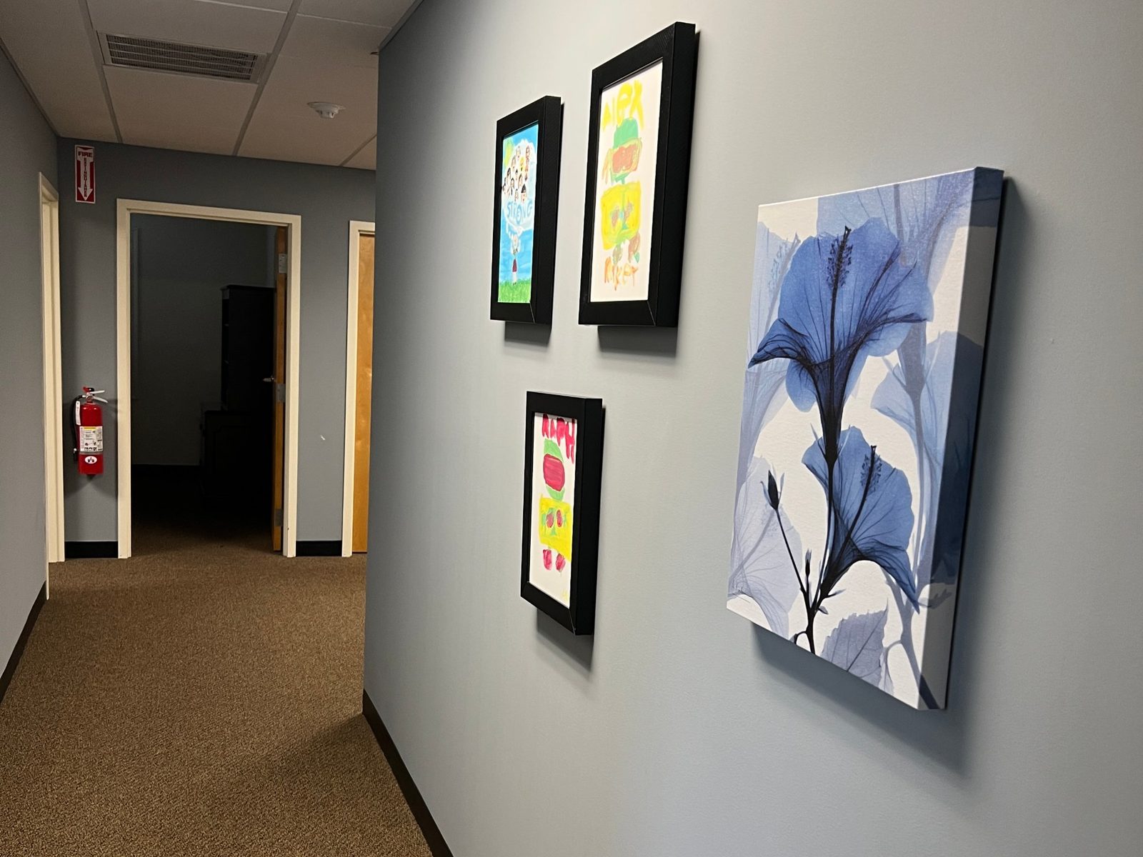 Hallway wall with framed children's drawings and a blue hibiscus print