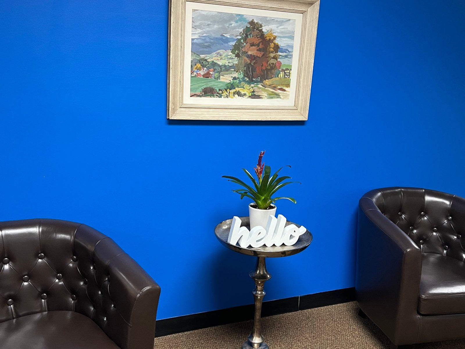 Seating area with leather club chairs against a bright blue wall and a hello sign