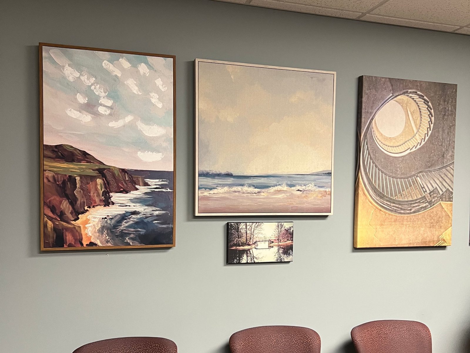Waiting room with upholstered chairs beneath three coastal paintings